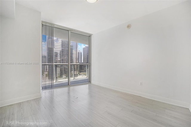 empty room with baseboards, floor to ceiling windows, a city view, and wood finished floors