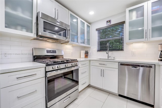 kitchen with tasteful backsplash, glass insert cabinets, light tile patterned floors, stainless steel appliances, and a sink