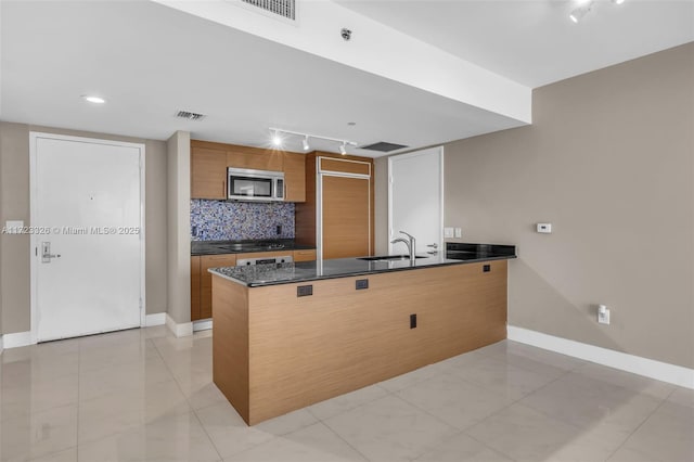 kitchen with sink, kitchen peninsula, dark stone counters, decorative backsplash, and light tile patterned flooring