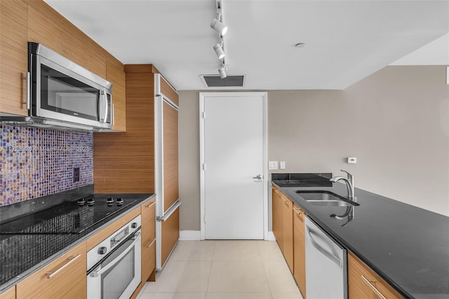 kitchen featuring sink, backsplash, track lighting, light tile patterned floors, and appliances with stainless steel finishes