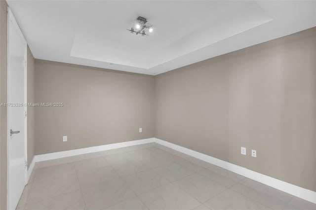 empty room with light tile patterned floors and a tray ceiling