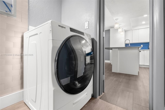 clothes washing area with washer / dryer, light hardwood / wood-style floors, and sink