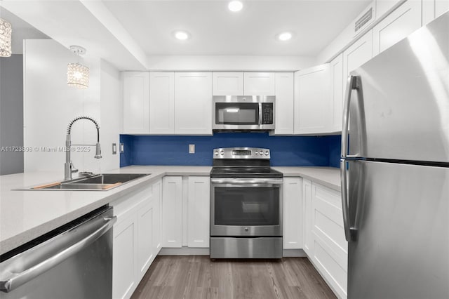 kitchen with sink, decorative light fixtures, light hardwood / wood-style floors, white cabinetry, and stainless steel appliances