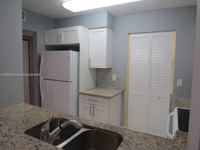 kitchen featuring white cabinets, sink, white fridge, and a textured ceiling