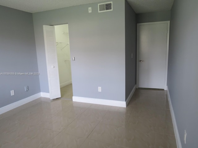 unfurnished room with baseboards, a textured ceiling, visible vents, and light tile patterned floors