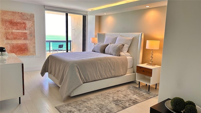 bedroom featuring access to outside, light wood-type flooring, floor to ceiling windows, and a water view