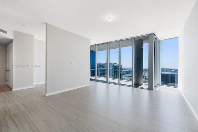 empty room with floor to ceiling windows and light hardwood / wood-style floors