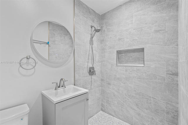 bathroom featuring toilet, tiled shower, and vanity