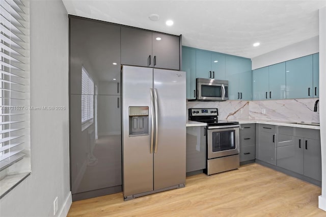 kitchen with light hardwood / wood-style floors, stainless steel appliances, blue cabinetry, and backsplash