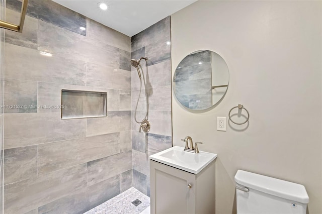 bathroom with a tile shower, vanity, and toilet