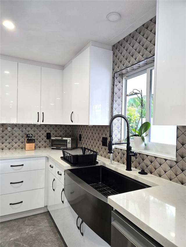 kitchen featuring decorative backsplash, stainless steel dishwasher, white cabinets, and sink