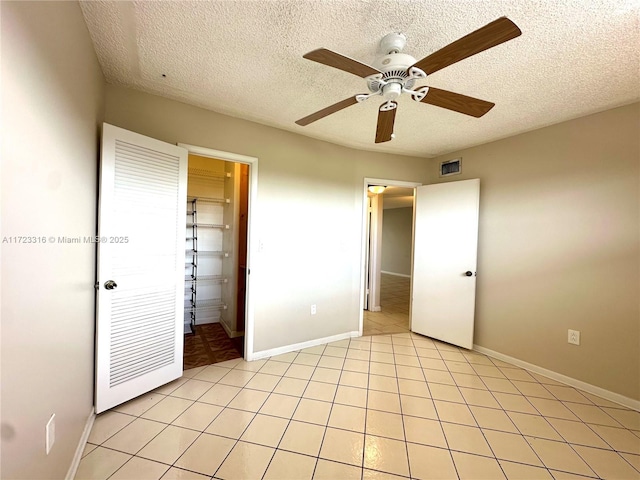 unfurnished bedroom with ceiling fan, a textured ceiling, connected bathroom, light tile patterned flooring, and a closet