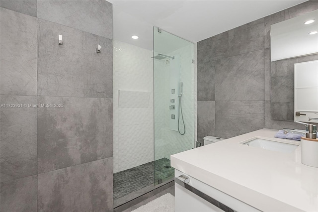 bathroom featuring vanity, toilet, a shower with door, and tile walls