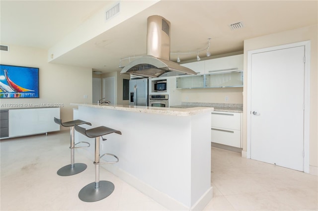 kitchen featuring appliances with stainless steel finishes, a breakfast bar area, white cabinetry, and island range hood