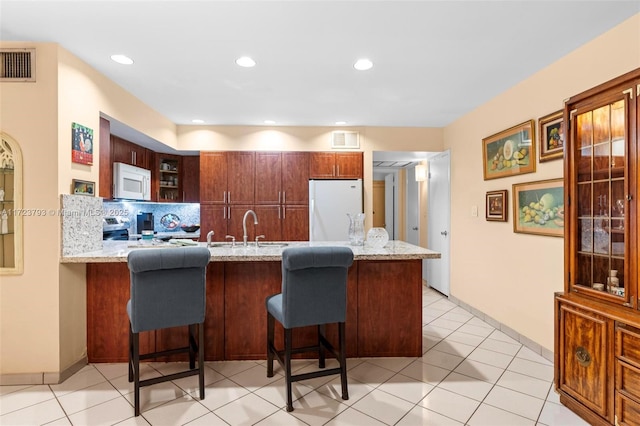 kitchen featuring sink, a kitchen bar, white appliances, and kitchen peninsula