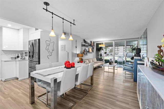 dining room with a textured ceiling, rail lighting, light hardwood / wood-style flooring, and a wall of windows