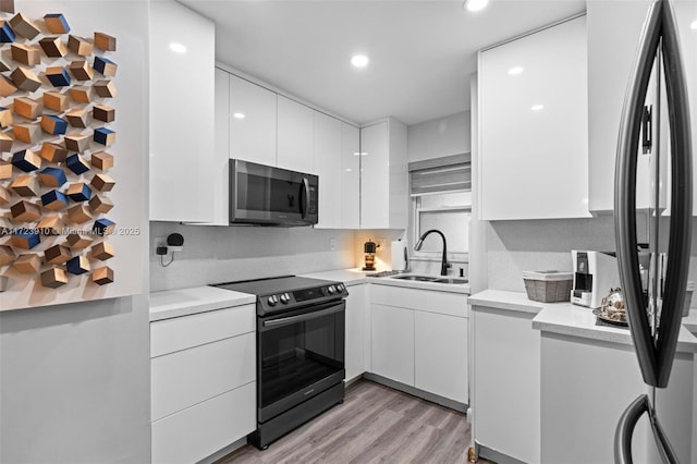 kitchen featuring white cabinets, black range with electric stovetop, sink, fridge, and light hardwood / wood-style floors