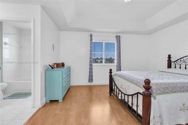 bedroom featuring a raised ceiling, ensuite bathroom, and light hardwood / wood-style floors