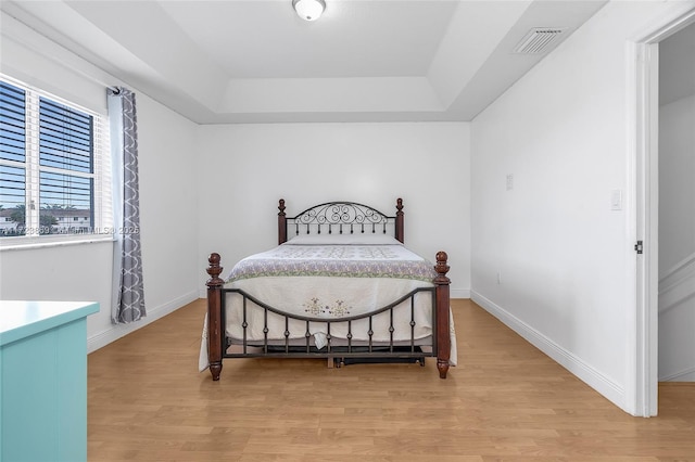 bedroom with a raised ceiling and light wood-type flooring