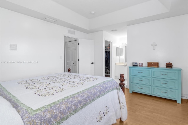 bedroom featuring a raised ceiling, a walk in closet, a closet, and light hardwood / wood-style floors