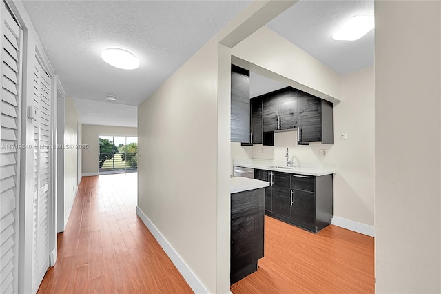 hall with sink, light hardwood / wood-style floors, and a textured ceiling