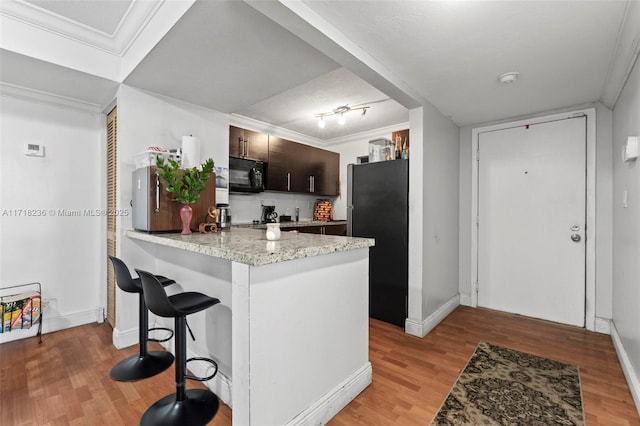 kitchen with kitchen peninsula, a kitchen bar, refrigerator, dark brown cabinetry, and light hardwood / wood-style flooring