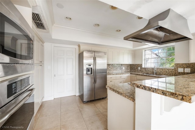 kitchen featuring sink, stainless steel appliances, a raised ceiling, island exhaust hood, and kitchen peninsula