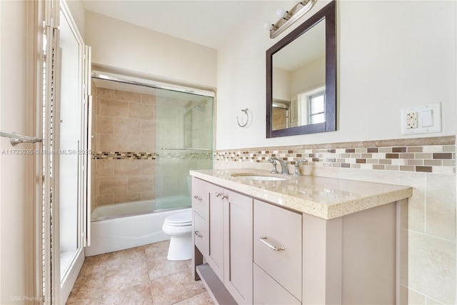 full bathroom featuring vanity, shower / bath combination with glass door, tile walls, tile patterned flooring, and toilet