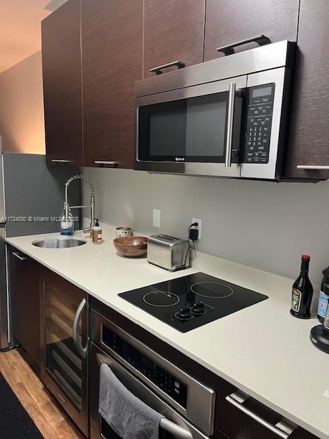 kitchen featuring dark brown cabinets, light wood-type flooring, stainless steel appliances, and sink