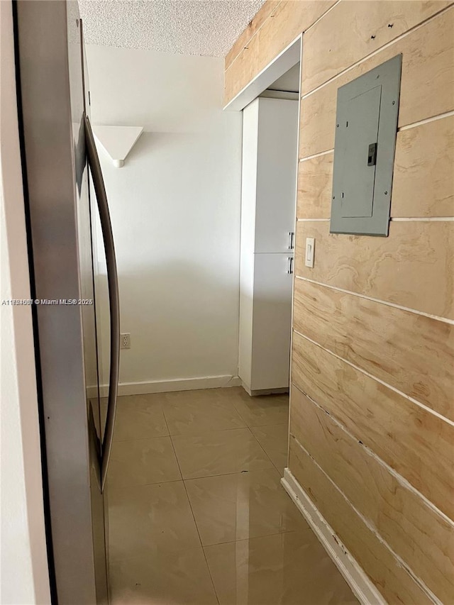 hallway featuring light tile patterned floors, a textured ceiling, electric panel, and wood walls