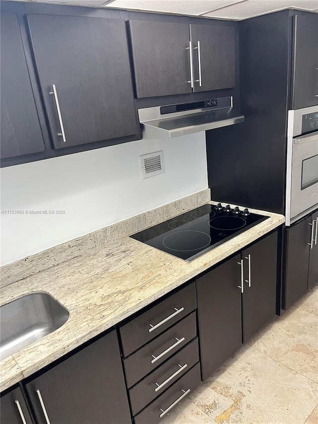 kitchen featuring ventilation hood, oven, sink, black electric cooktop, and light stone counters