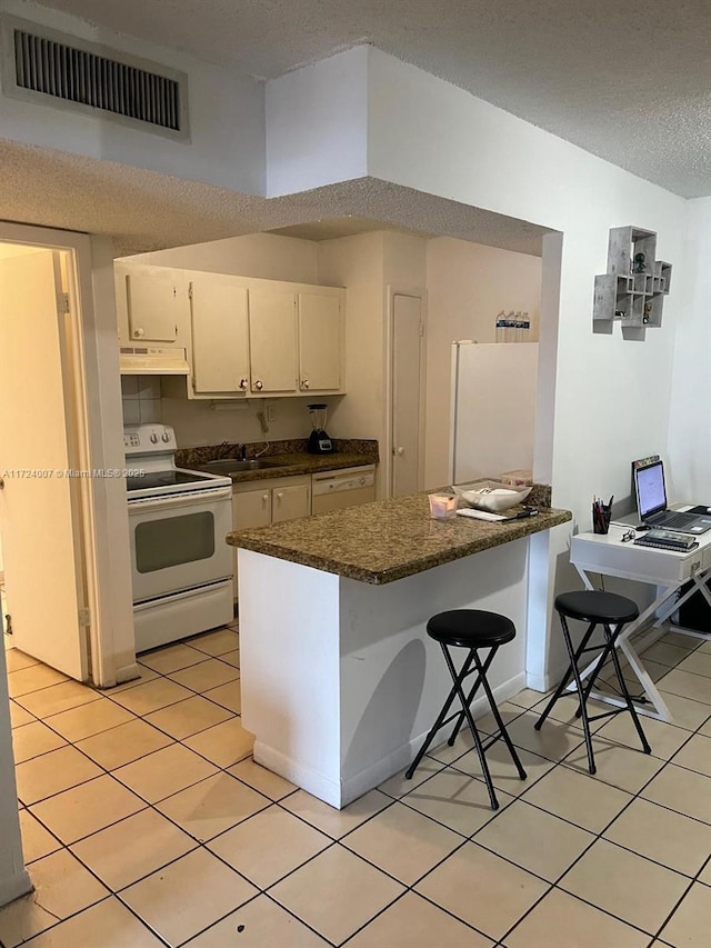 kitchen featuring white appliances, light tile patterned floors, a textured ceiling, white cabinetry, and a breakfast bar area