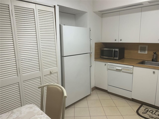 kitchen with light tile patterned floors, white appliances, a sink, visible vents, and white cabinetry