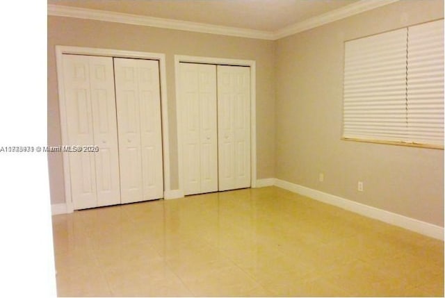 unfurnished bedroom featuring tile patterned flooring, ornamental molding, and multiple closets