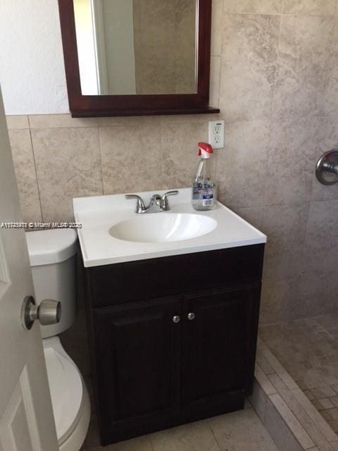 bathroom featuring a tile shower, vanity, and toilet