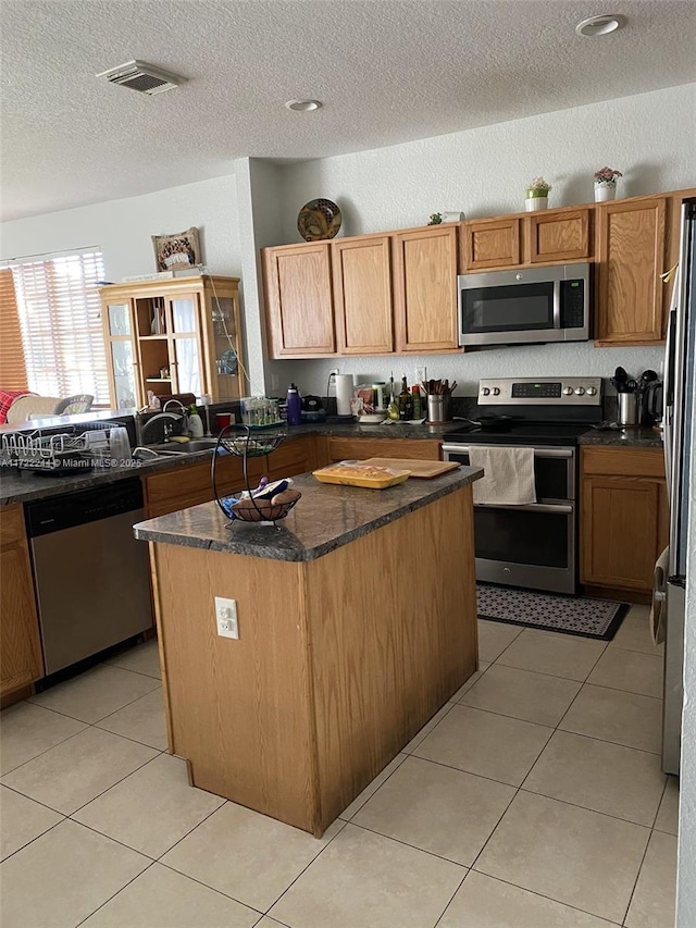 kitchen with light tile patterned floors, a textured ceiling, appliances with stainless steel finishes, and a center island