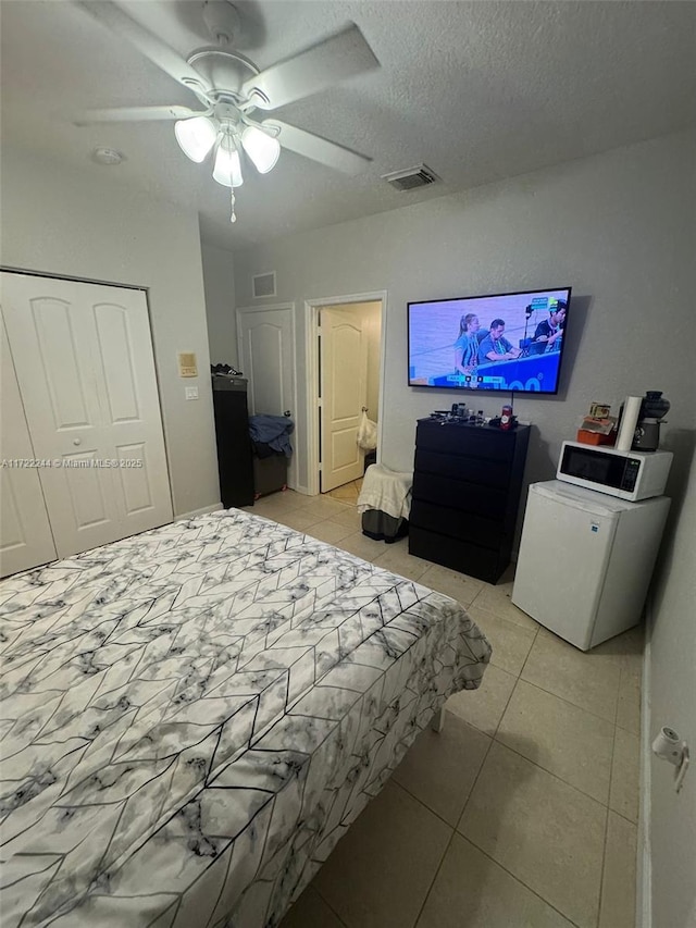 bedroom featuring ceiling fan, light tile patterned floors, and a textured ceiling