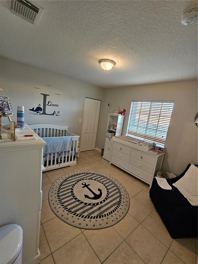 bedroom with a textured ceiling, a crib, and light tile patterned flooring