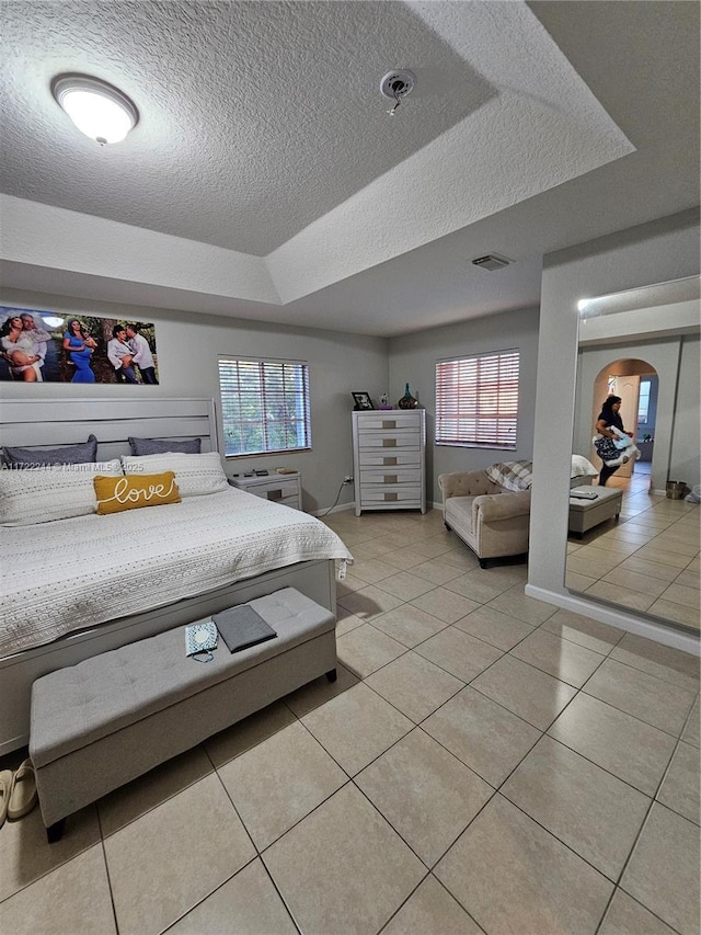 bedroom with multiple windows, a tray ceiling, and light tile patterned flooring