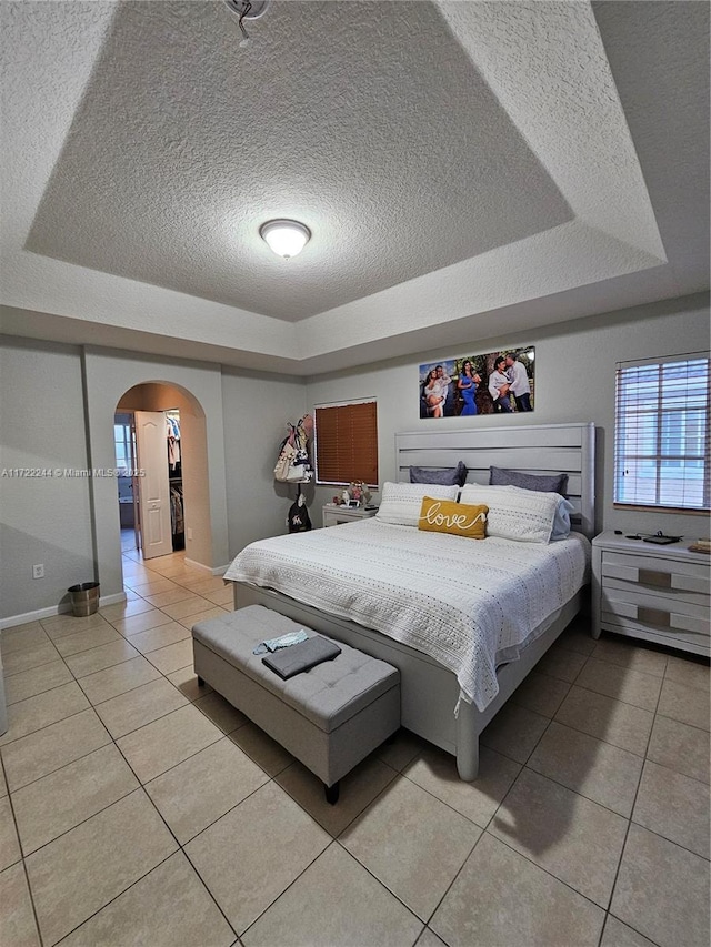 bedroom featuring a textured ceiling, a tray ceiling, and light tile patterned floors