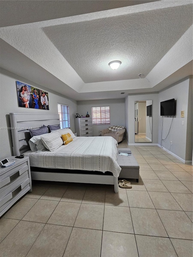 bedroom with a textured ceiling, a tray ceiling, and light tile patterned flooring