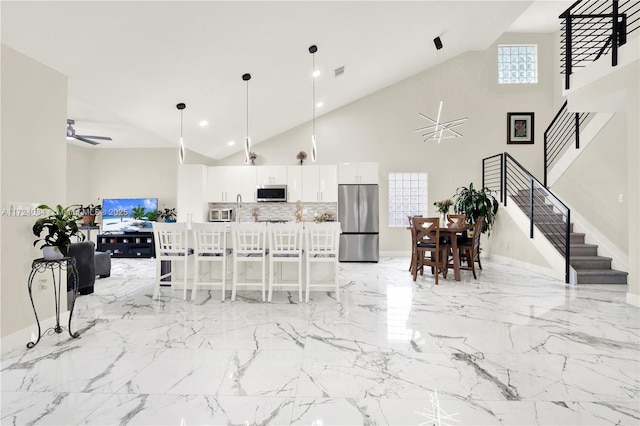 kitchen featuring ceiling fan, white cabinetry, high vaulted ceiling, a breakfast bar, and appliances with stainless steel finishes