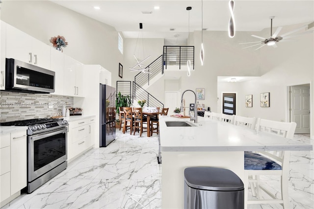 kitchen featuring pendant lighting, a high ceiling, a center island with sink, a kitchen breakfast bar, and stainless steel appliances