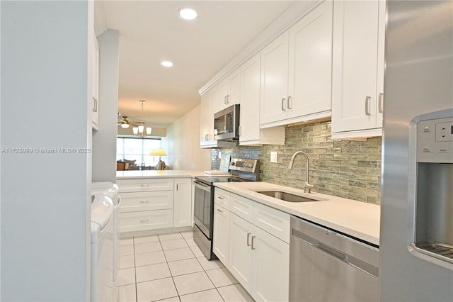 kitchen with appliances with stainless steel finishes, ceiling fan, washer and clothes dryer, sink, and white cabinets