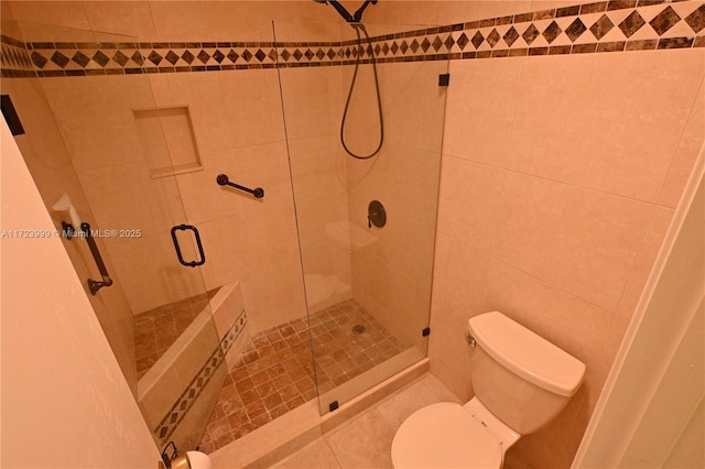 bathroom featuring toilet, a shower with door, and tile walls