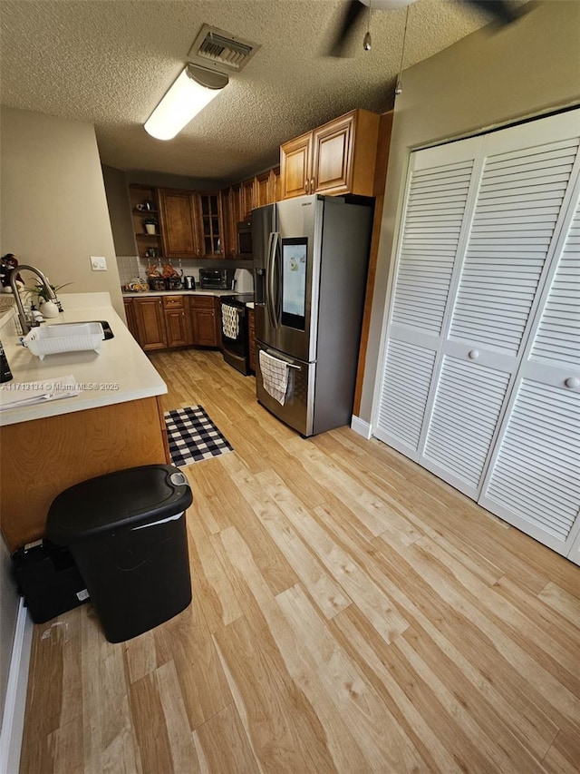 kitchen with sink, a textured ceiling, black / electric stove, light hardwood / wood-style floors, and stainless steel fridge with ice dispenser