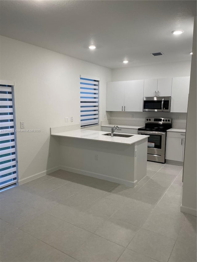 kitchen featuring sink, kitchen peninsula, light tile patterned flooring, white cabinetry, and stainless steel appliances