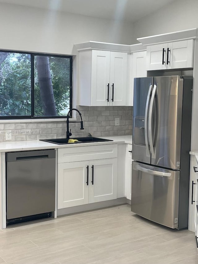 kitchen featuring backsplash, white cabinets, sink, light hardwood / wood-style floors, and stainless steel appliances