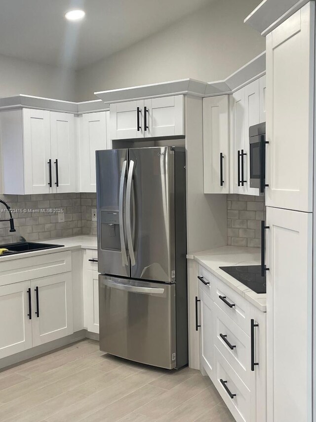 kitchen featuring white cabinetry, sink, tasteful backsplash, stainless steel fridge, and black electric cooktop