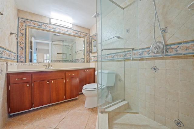 bathroom with vanity, a shower with door, tile patterned floors, toilet, and tile walls